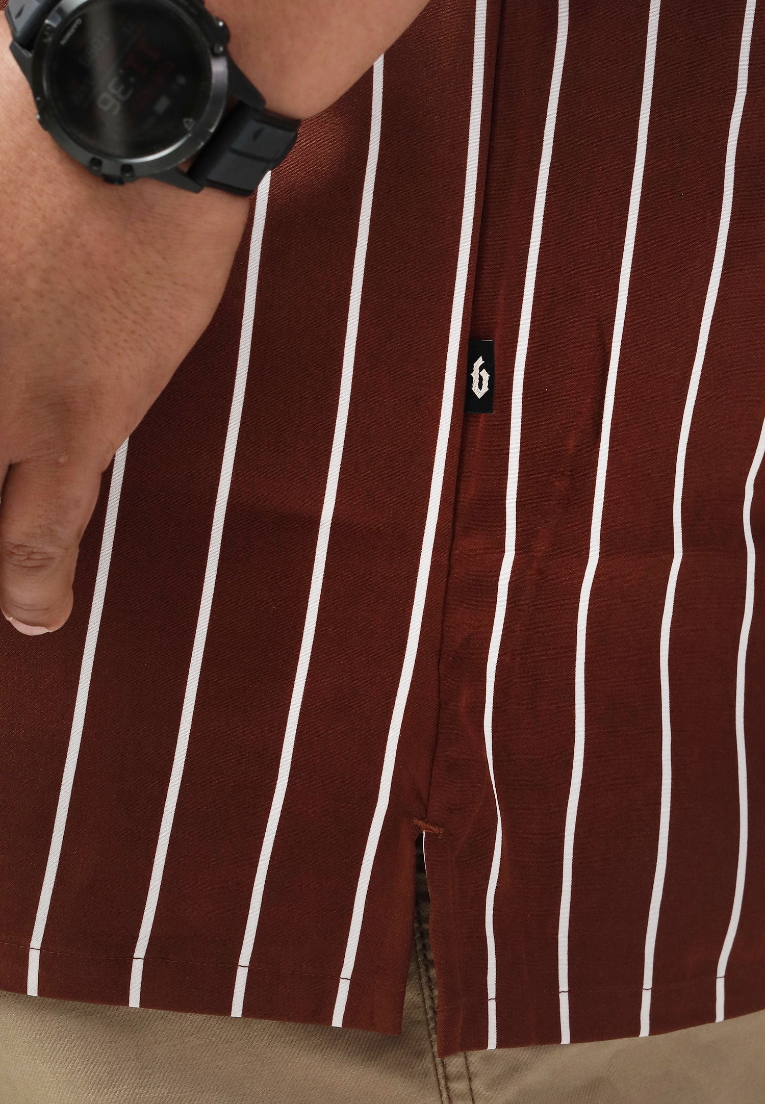 A close-up of the slit with a 'B' flag tag logo on a brown shirt with white stripes. #color_brown